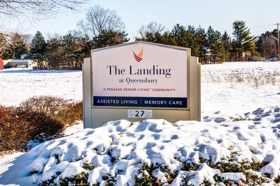 A sign for The Landing at Queensbury, an assisted living and memory care facility, covered in snow.