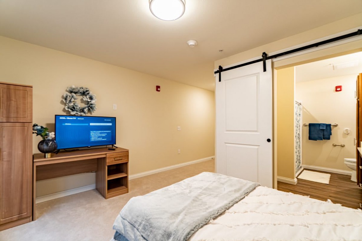 A cozy bedroom featuring a bed, television on a desk, and a sliding barn door leading to another room.