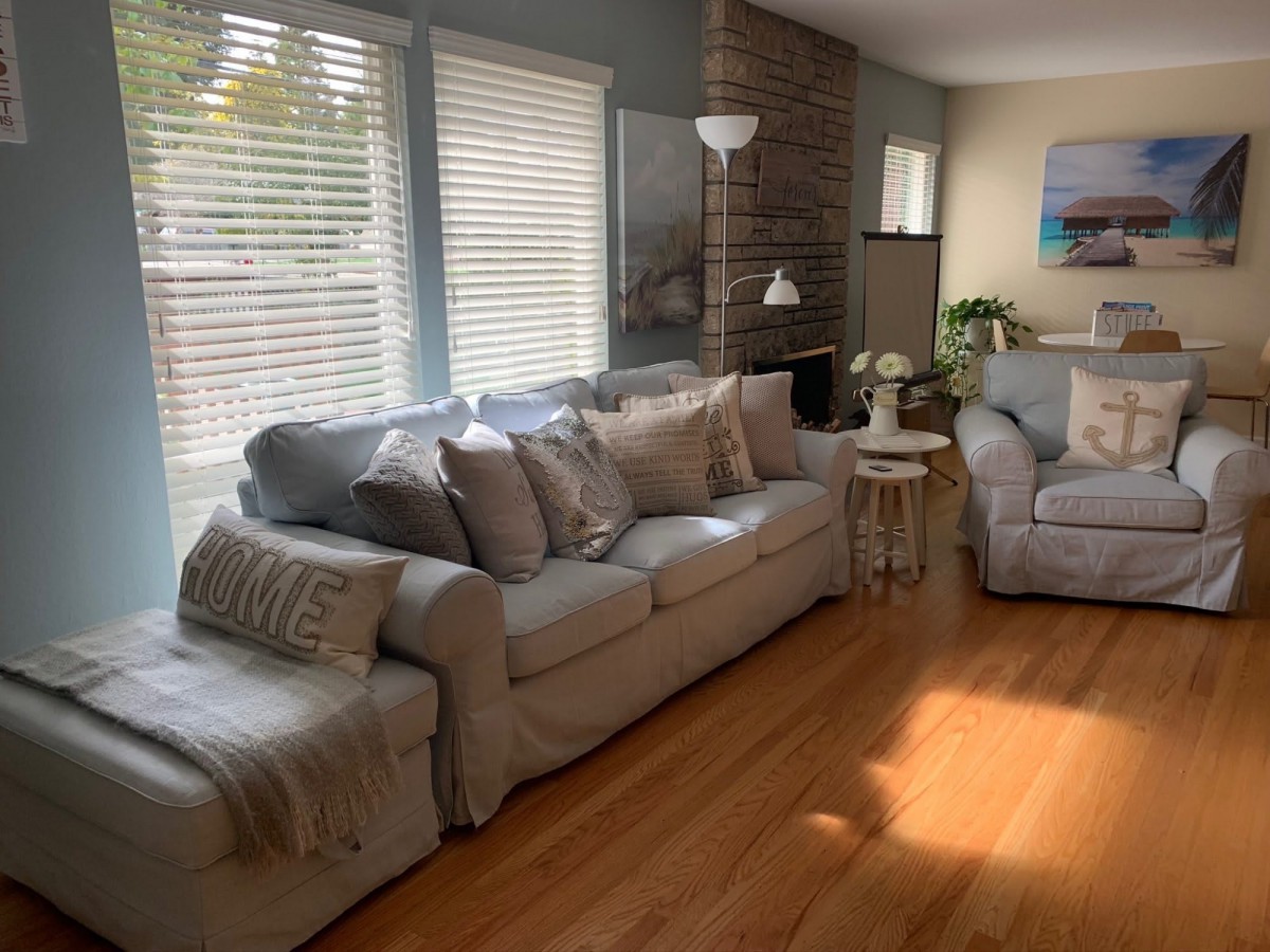 A cozy living room with a large sofa, wooden floors, and ample natural light.