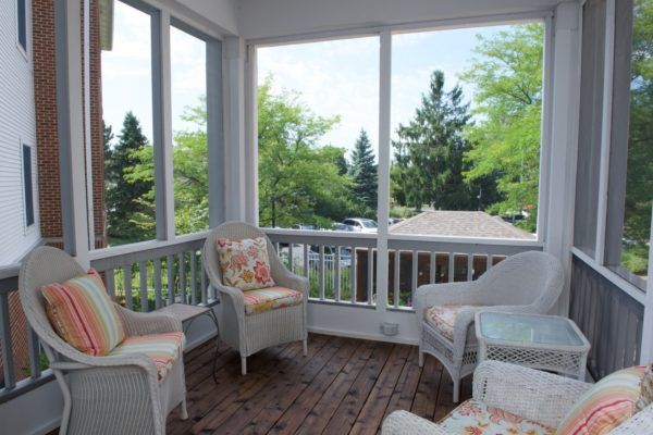 A cozy screened porch with wicker furniture and a view of lush greenery.