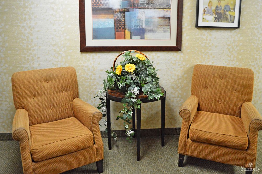 A cozy waiting room with two orange chairs, a side table with a floral arrangement, and artwork on the wall.