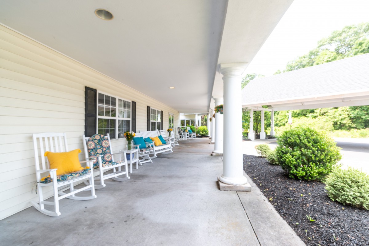 A covered porch with rocking chairs and colorful pillows, surrounded by greenery.