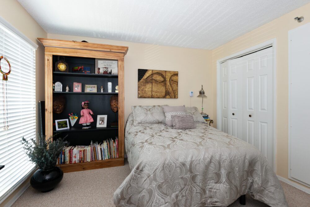 A cozy bedroom with a bed, bookshelves filled with decor and books, and artwork on the walls.