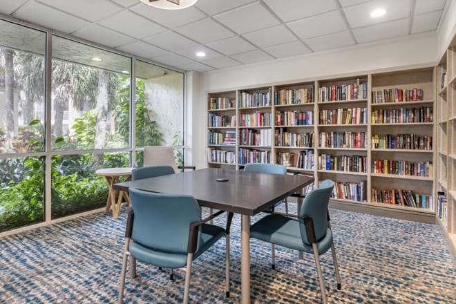 A cozy study room with bookshelves, a table, and chairs by a large window.