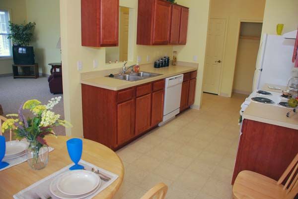 A kitchen with wooden cabinets, a sink, and a dishwasher, adjacent to a small dining area with table settings.