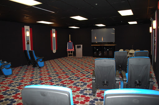 An empty room designed for presentations or gatherings, featuring a projector screen and patterned carpet.