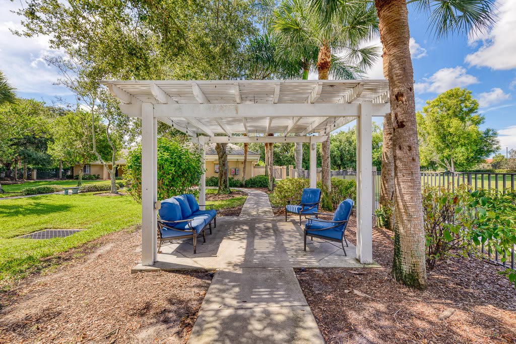 A tranquil garden setting with a white pergola and blue cushioned chairs, perfect for relaxation.