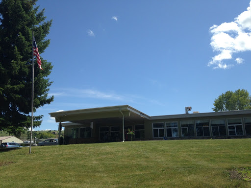 A modern building set against a clear blue sky, featuring a flag and well-manicured grass.
