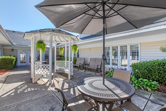 A cozy outdoor patio area with a table, chairs, umbrella, and a gazebo surrounded by plants.