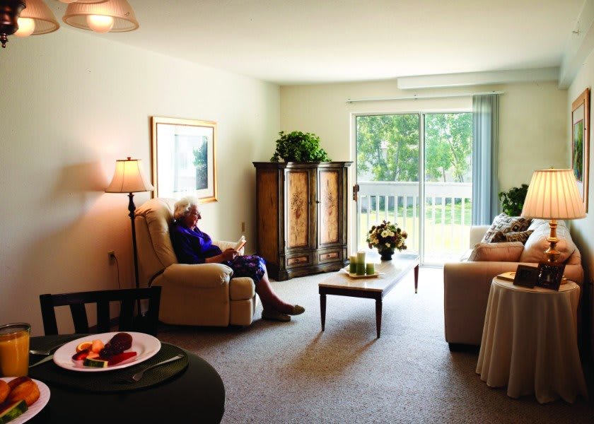 A cozy living room with a person sitting in an armchair near a large window.