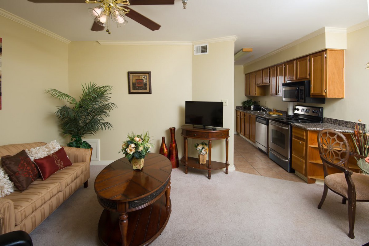 A cozy living room with a sofa, coffee table, and television, leading into an open kitchen with modern appliances.