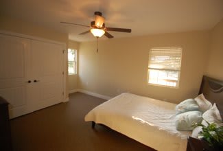 A minimalist bedroom with a ceiling fan, bed, and ample natural light.