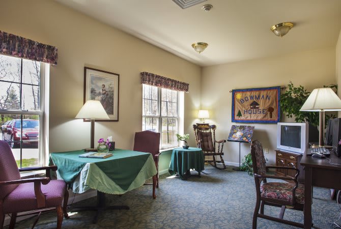 A cozy living room with chairs and tables, decorated with lamps and artwork.