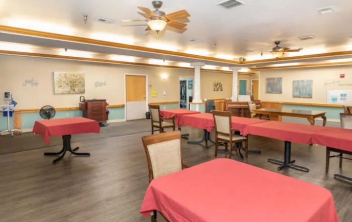 A spacious dining room with red tablecloths, wooden chairs, and ceiling fans.