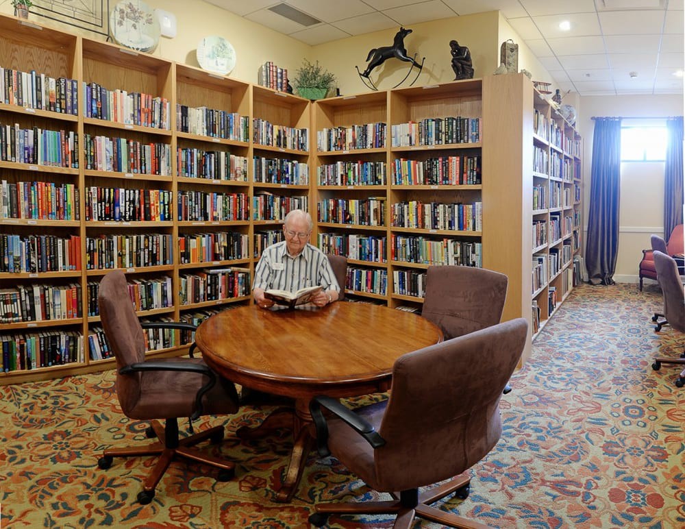 A person reading a book at a round table in a cozy library.