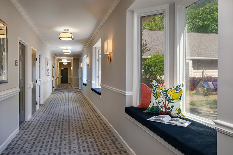 A bright, well-decorated hallway featuring large windows and comfortable seating.