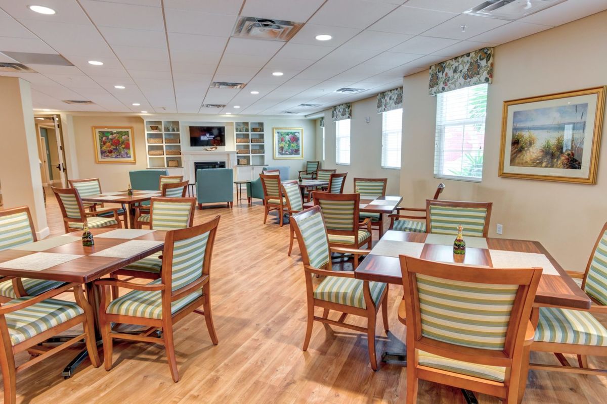 An inviting dining area with wooden floors, multiple tables and chairs, and natural light streaming through the windows.