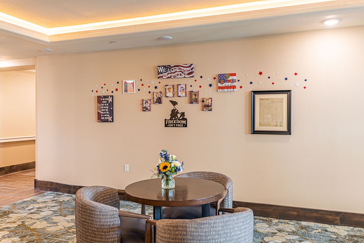 A cozy room with a round table and chairs, featuring wall art and a vase of flowers.