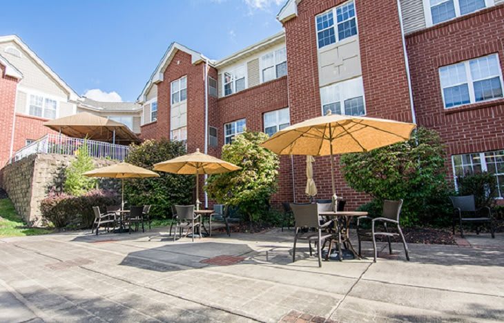 A sunny outdoor patio with tables, chairs, and umbrellas in front of a brick building.