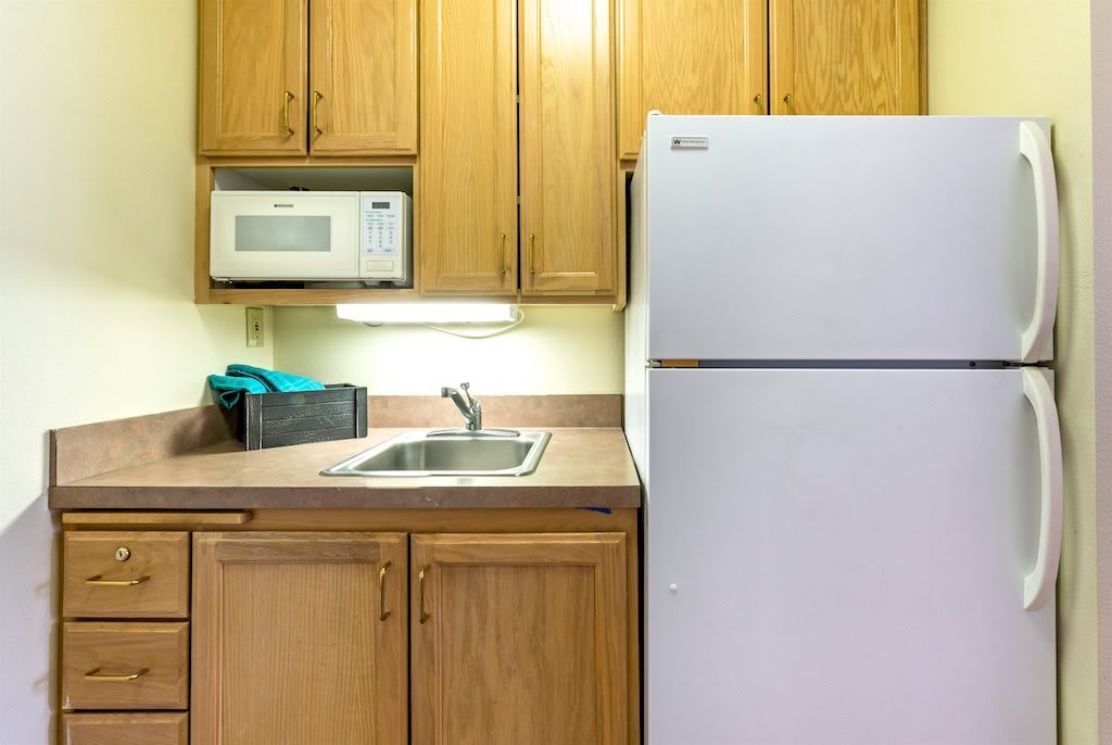 A compact kitchen area with a refrigerator, microwave, sink, and wooden cabinets.