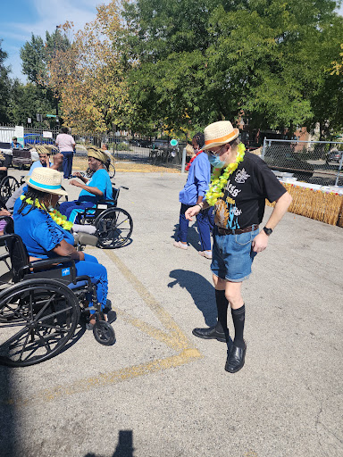 A vibrant outdoor gathering featuring attendees in wheelchairs wearing leis and hats, enjoying a sunny day.