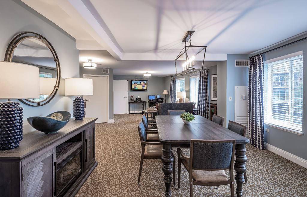 A modern dining room featuring a long wooden table with upholstered chairs, decorative mirrors, and contemporary lighting fixtures.