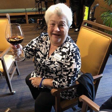A smiling woman holding a wine glass while sitting indoors.