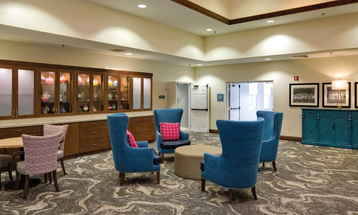A welcoming lobby area with comfortable blue chairs and a round table, enhanced by soft lighting and a patterned carpet.