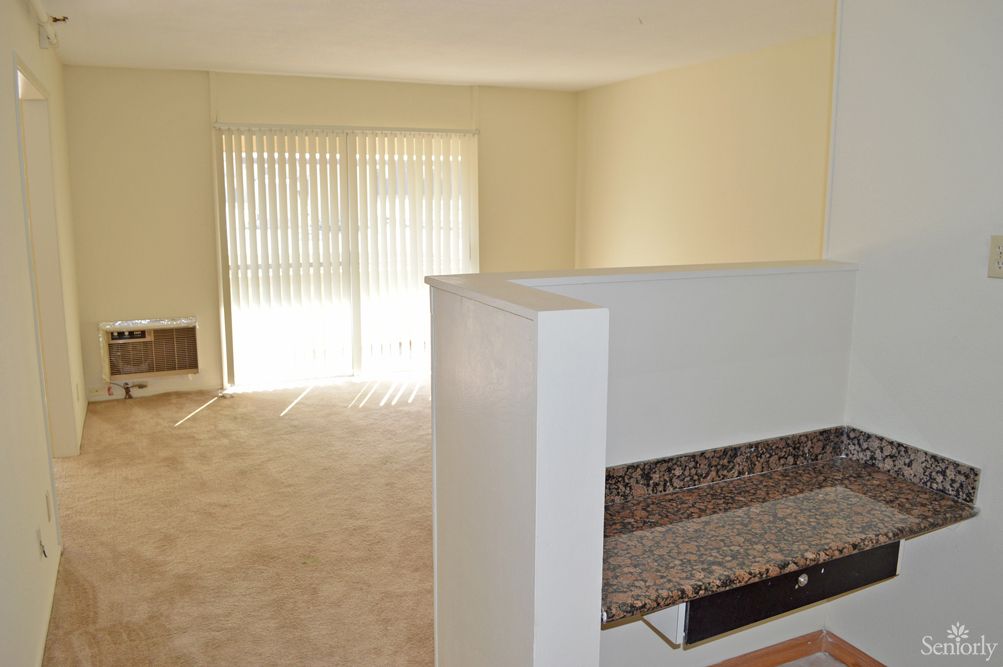 A minimalist apartment living room featuring carpeted flooring and large sliding glass doors that let in natural light.