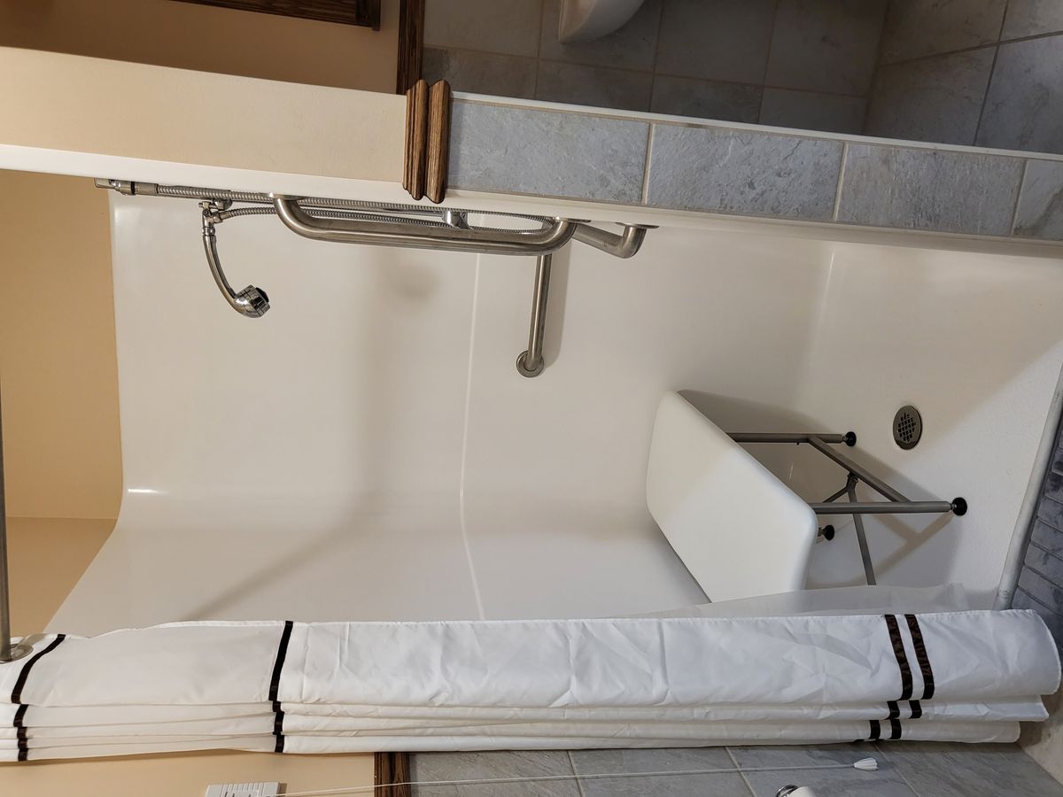 An accessible bathroom with a bathtub, shower area, grab bars, and a bath chair.