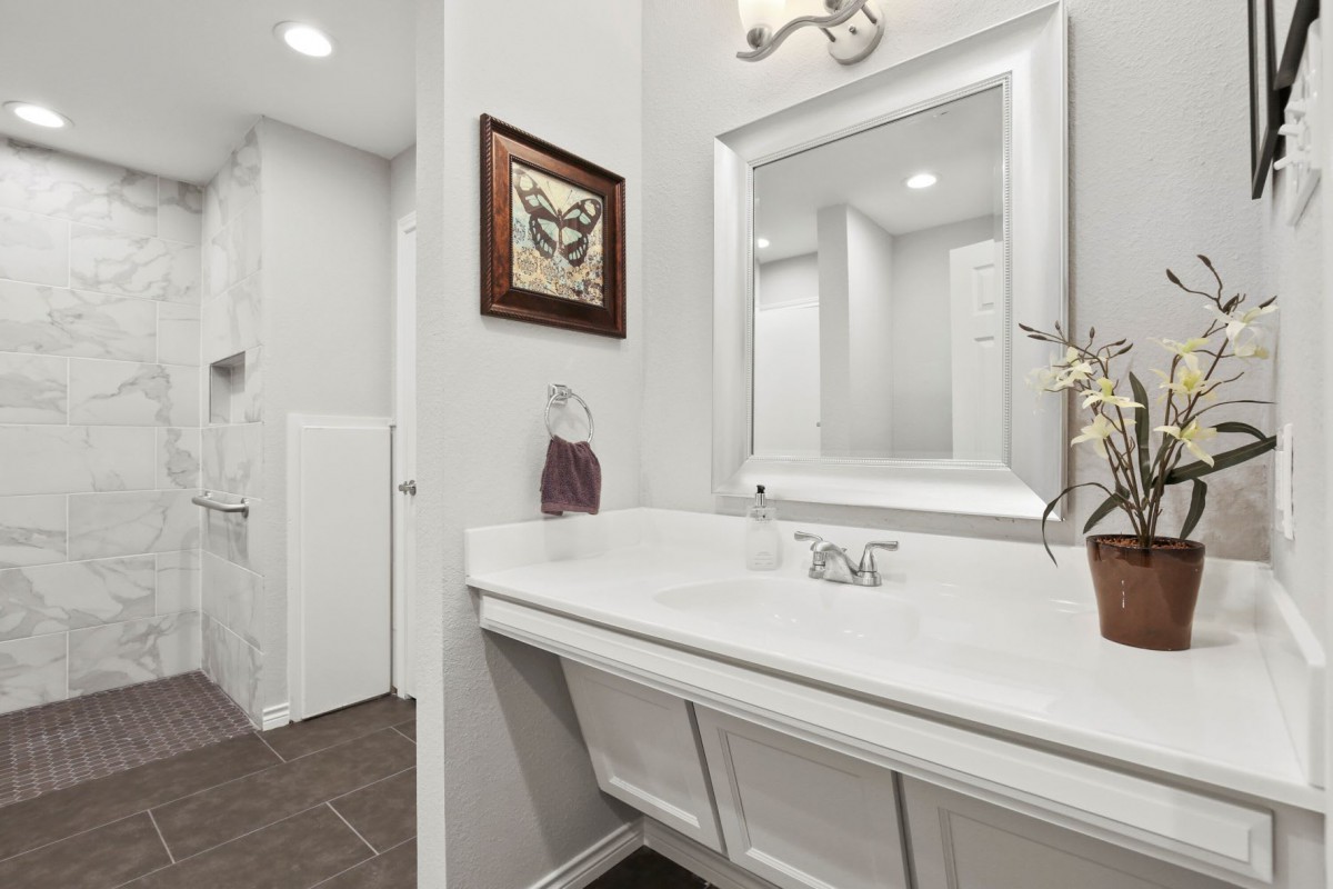 A modern bathroom featuring a large mirror above a sleek white sink, with minimalist decor and framed artwork.