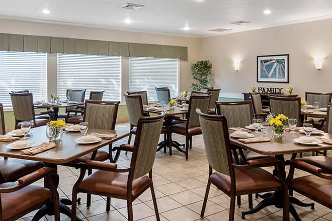 An empty dining room with neatly arranged tables and chairs, featuring large windows and bright lighting.