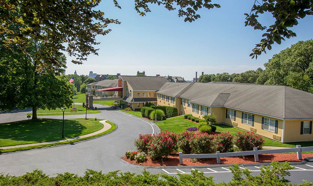 A scenic view of a hotel building surrounded by landscaped greenery and parking area under a clear blue sky.
