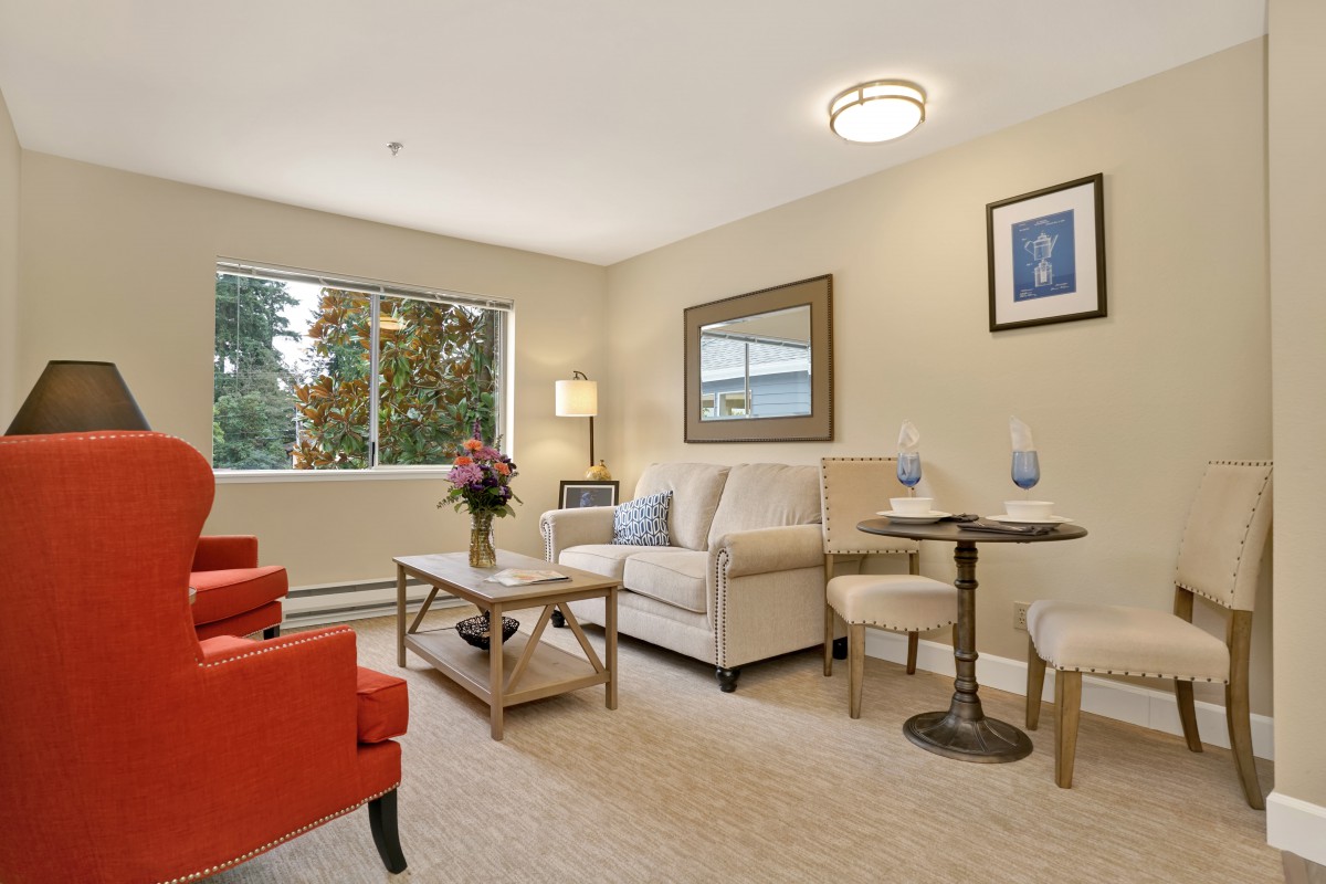 A cozy and well-decorated living room with a sofa, chairs, and a window overlooking greenery.