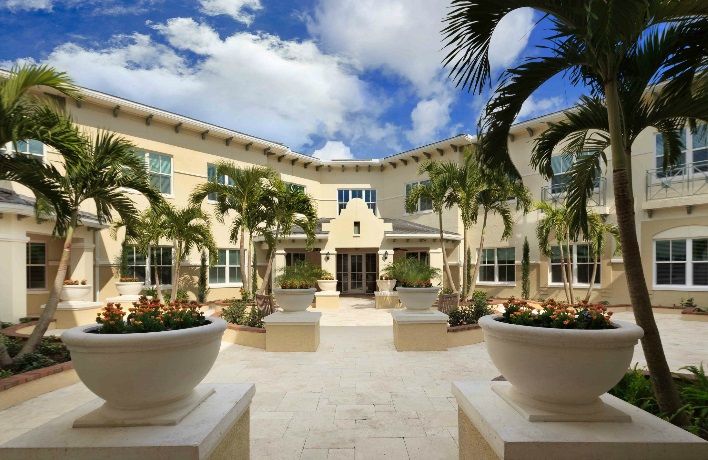 A beautiful courtyard featuring a modern building facade with palm trees and a clear blue sky.