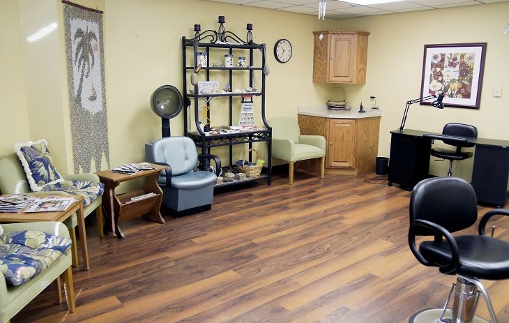 A cozy salon interior with seating, hair dryer, and a wooden floor.