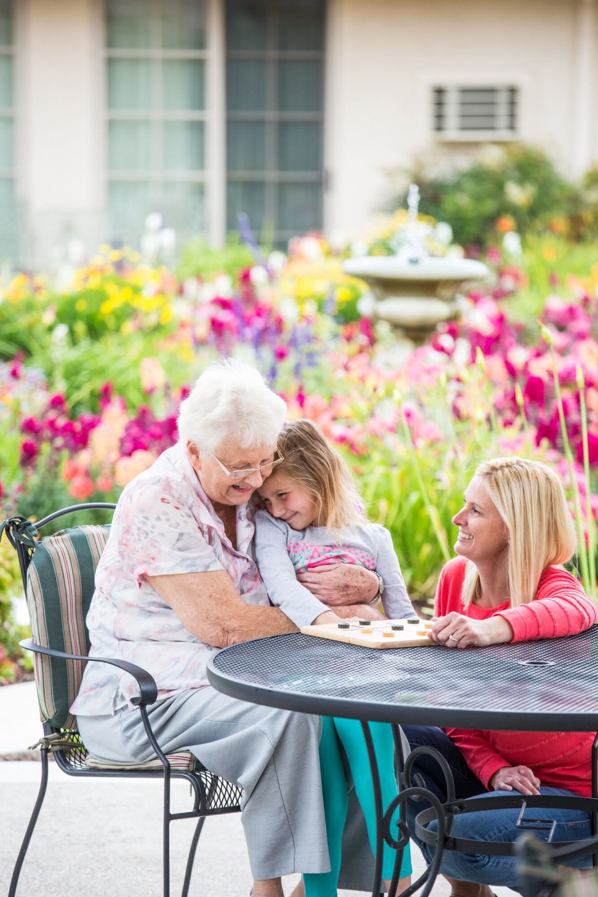 A joyful family moment in a colorful garden, with three generations bonding over a game at an outdoor table.