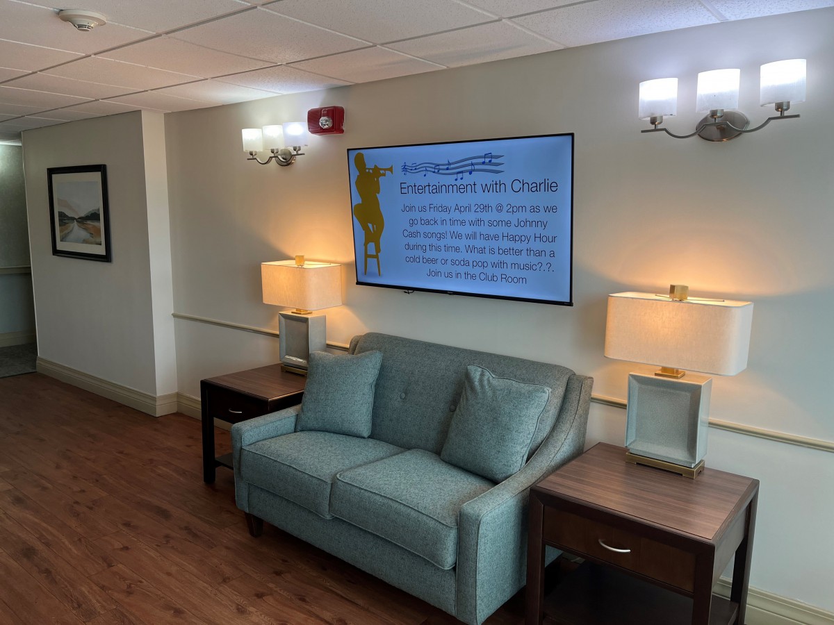 A cozy lobby area with a couch, lamps, and a large television displaying information.