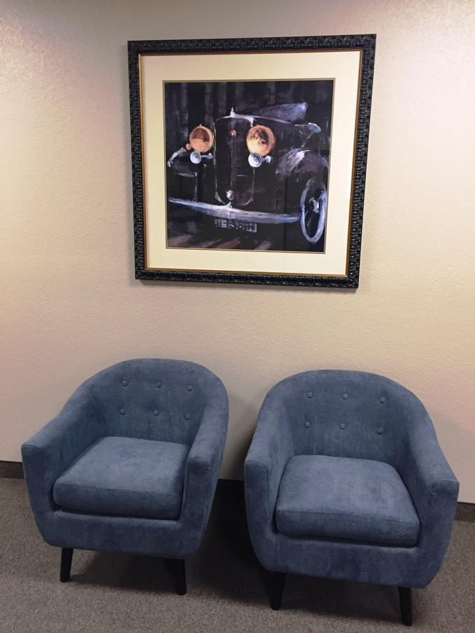 Two blue chairs beneath a framed painting of a vintage car.
