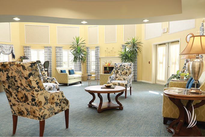 A cozy and well-decorated living room with floral chairs, a coffee table, and potted plants.