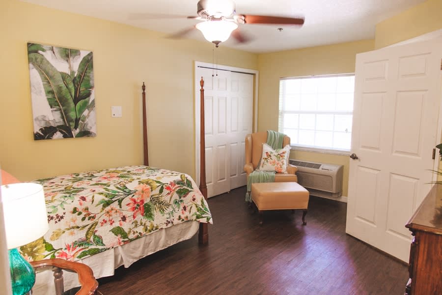 A cozy bedroom with a floral bedspread, armchair, and closet.