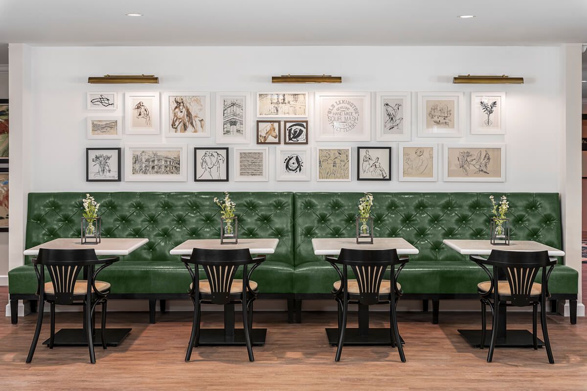 A stylish restaurant interior with green upholstered seating and framed artwork on the walls.