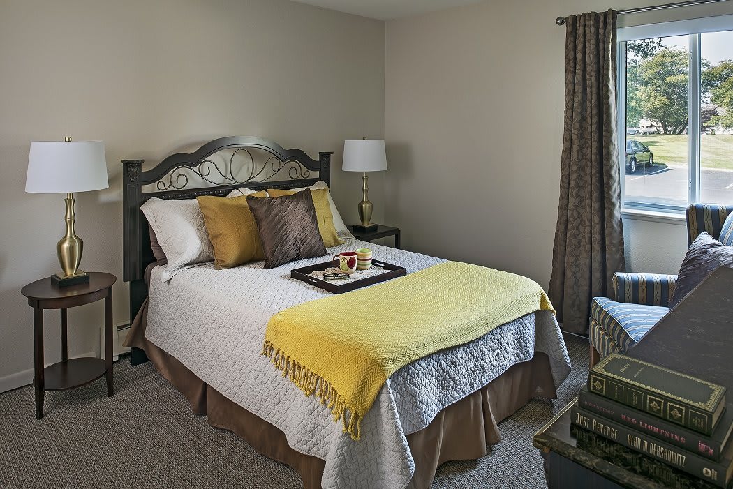 A cozy bedroom with a neatly made bed featuring decorative pillows and a yellow blanket, accompanied by a nightstand with a lamp and tray.
