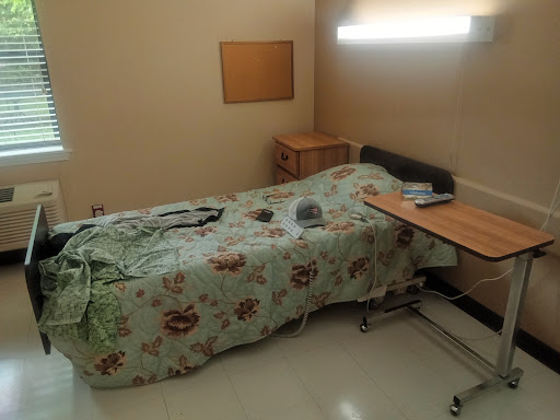 A tidy hospital room featuring a patient bed with floral bedding and a simple wooden bedside table.