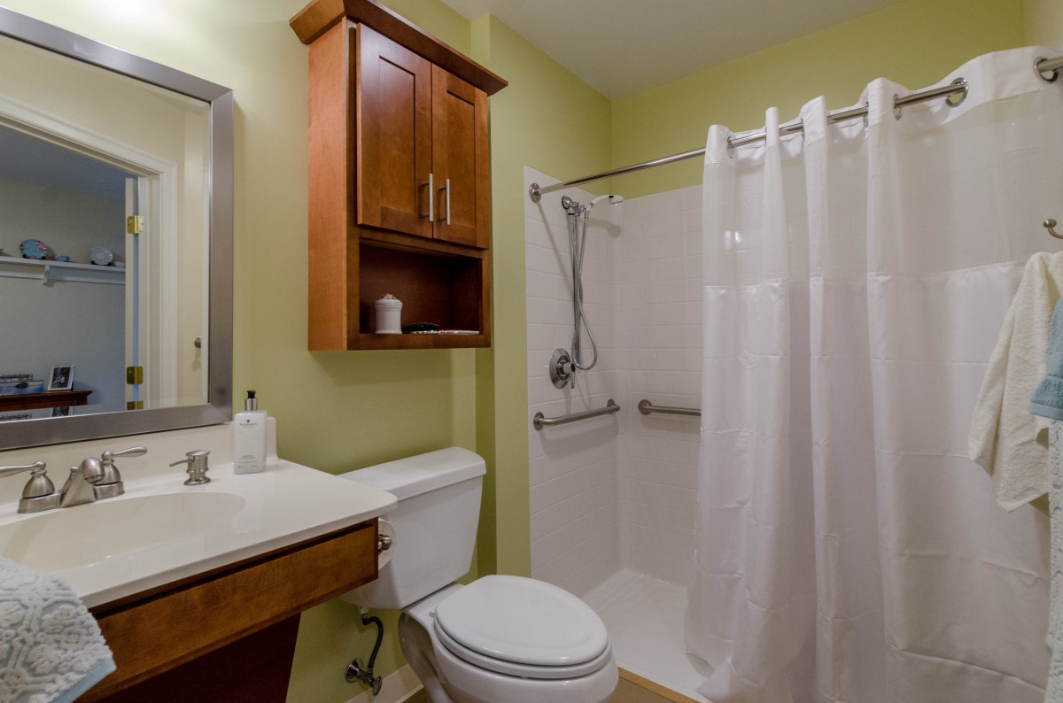 A small, neatly arranged bathroom featuring a shower with a curtain, a toilet, and a sink with a mirror and cabinet.