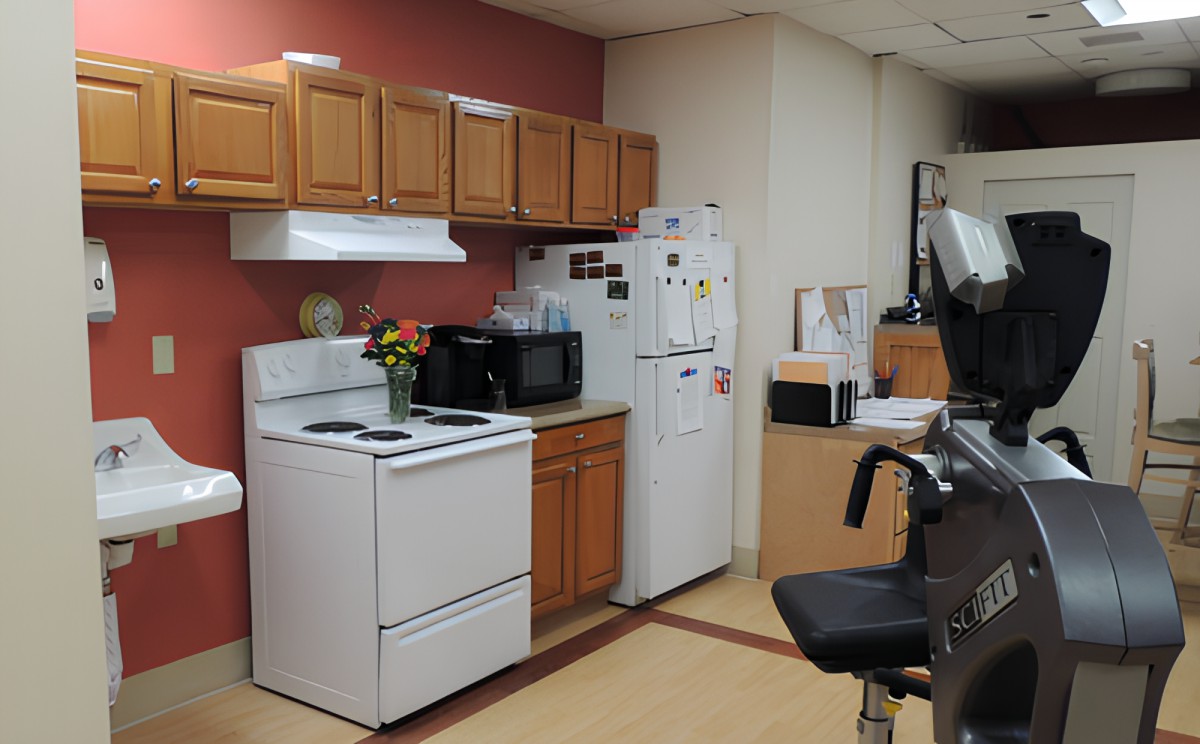 An office kitchen area with a stove, refrigerator, microwave, and wooden cabinets.