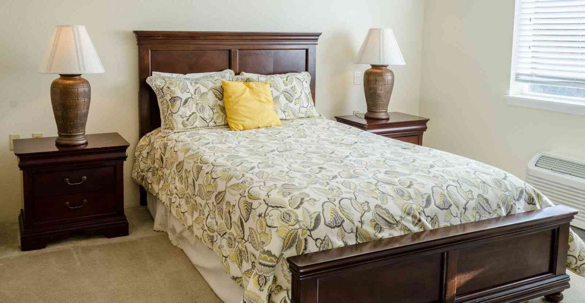 A cozy bedroom with a wooden bedframe, floral bedding, and a nightstand with a lamp.