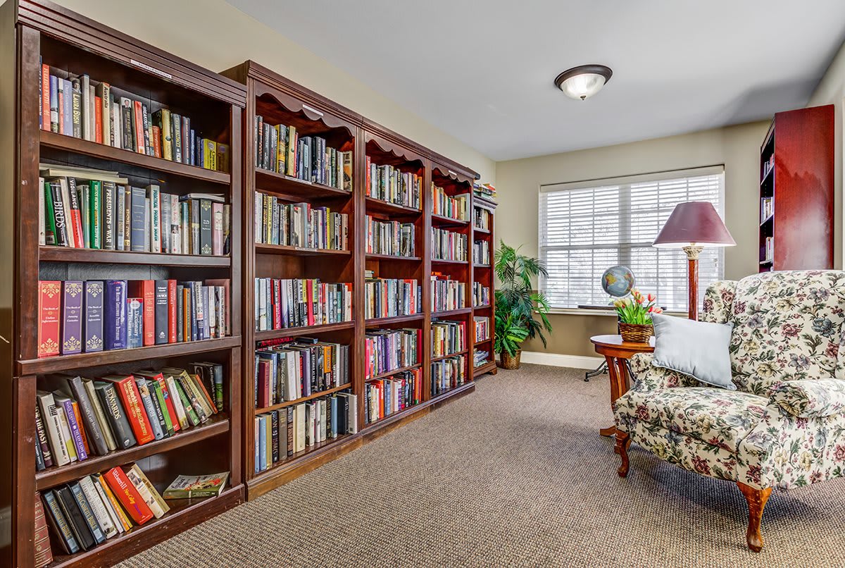 A cozy library corner featuring wooden bookshelves filled with books, a comfortable chair, and a large window letting in natural light.