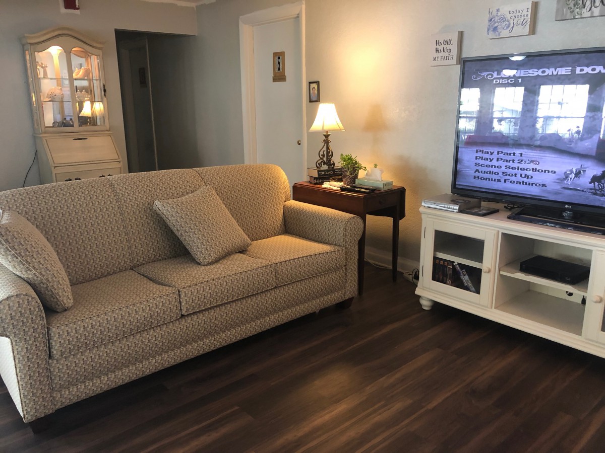 A cozy living room with a sofa, television, and lamp on hardwood flooring.
