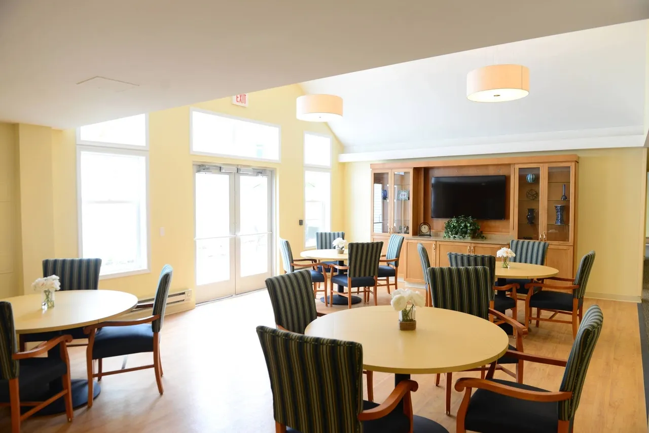 A bright and welcoming dining area with round tables, cushioned chairs, and a television in the background.